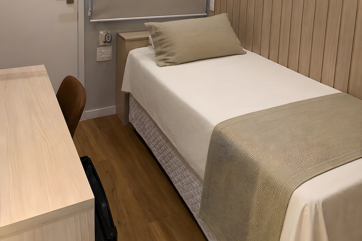 Una habitación de hotel pequeña con cama, mesita de noche, silla y escritorio.
