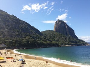 A beach with clear turquoise water, a large rock formation, and a sandy shore with people and umbrellas. - Catete Residence (Rio de Janeiro)
