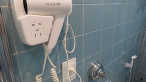 Um secador de cabelo fixado na parede, com uma tomada, um chuveiro metálico e uma torneira também na parede.