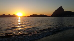 Um pôr do sol sobre um mar calmo, com o perfil de uma montanha ao fundo.