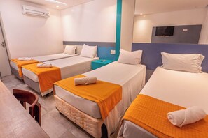 Une chambre d’hôtel avec trois lits simples, chacun recouvert d’une couverture orange et doté d’un oreiller blanc. On y trouve une petite table avec une chaise, une table de chevet et un téléviseur fixé au mur.