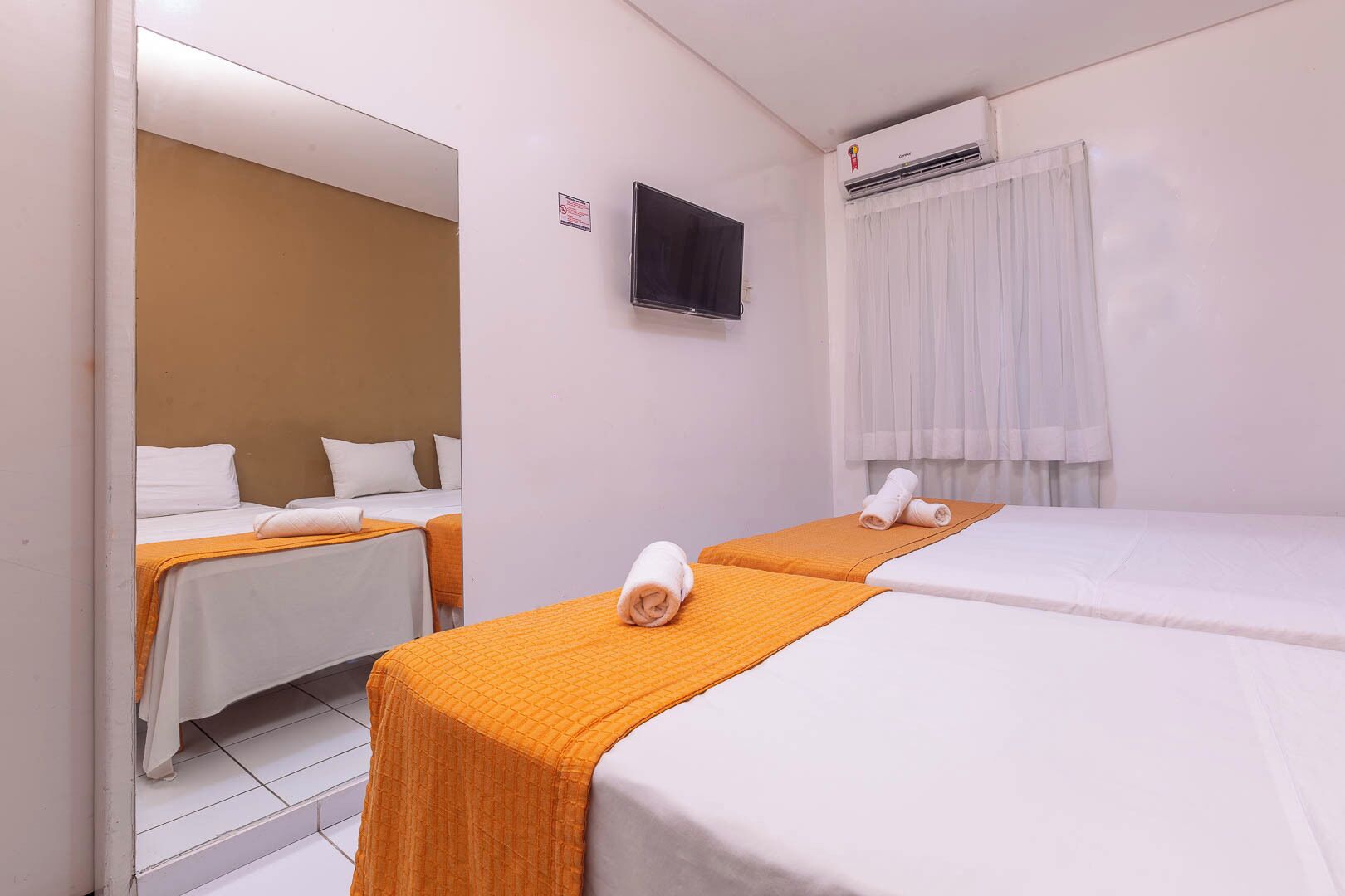 Une chambre d’hôtel avec deux lits, une télévision, un appareil de climatisation et un miroir.