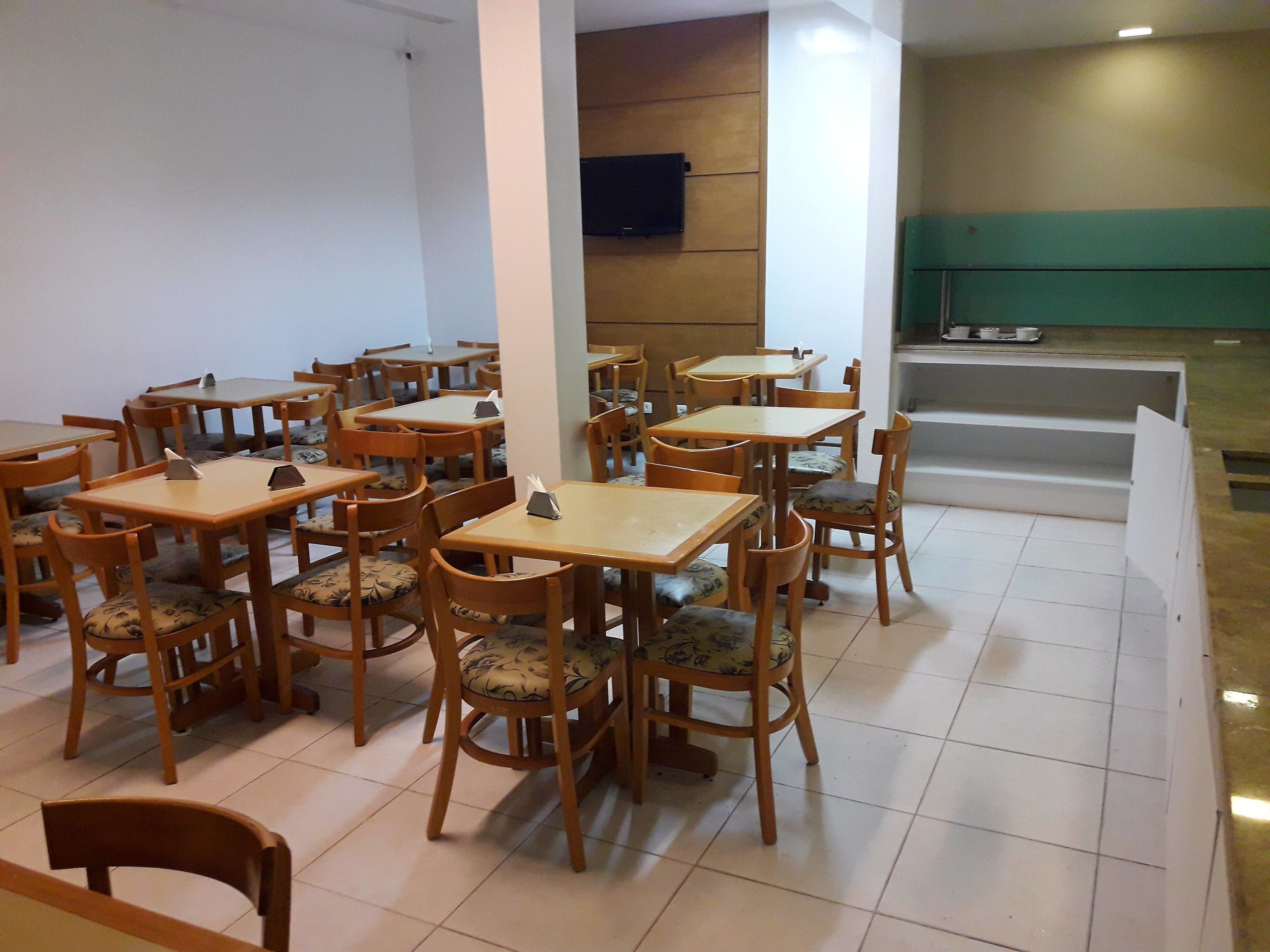 A dining area with multiple wooden tables and chairs, a flat-screen TV mounted on the wall, and a green wall in the background.