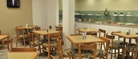 Un restaurante con mesas y sillas de madera, una barra con productos alimenticios y un televisor en la pared.