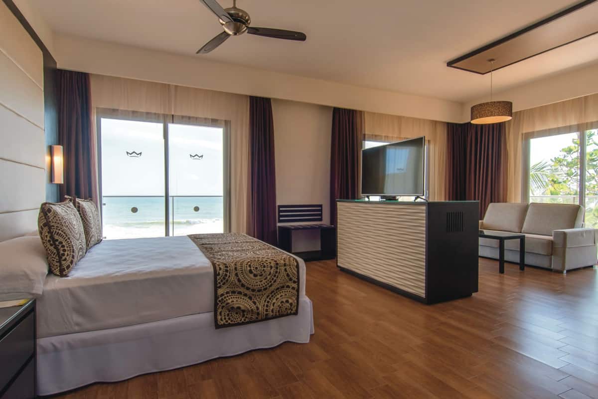 A hotel room with a bed, a desk, a TV, and a view of the ocean.