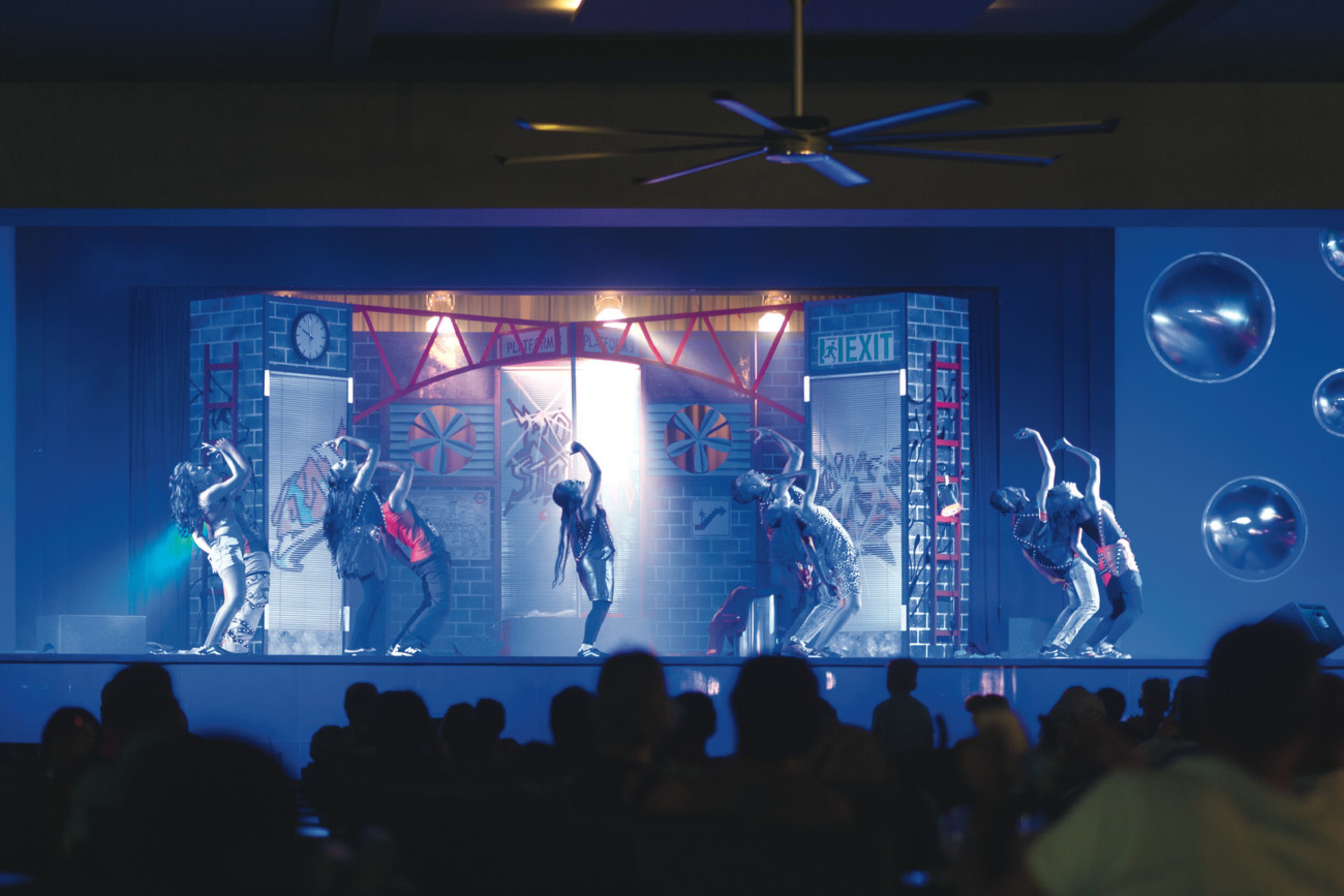A stage with performers, a ceiling fan, and a crowd.