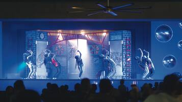A stage with performers, a ceiling fan, and a crowd.