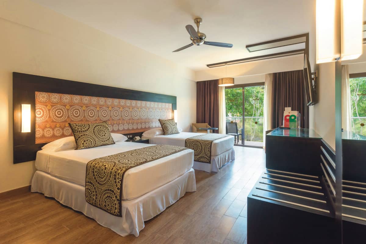 A hotel room with two beds, a ceiling fan, a desk, and a view of the outdoors.