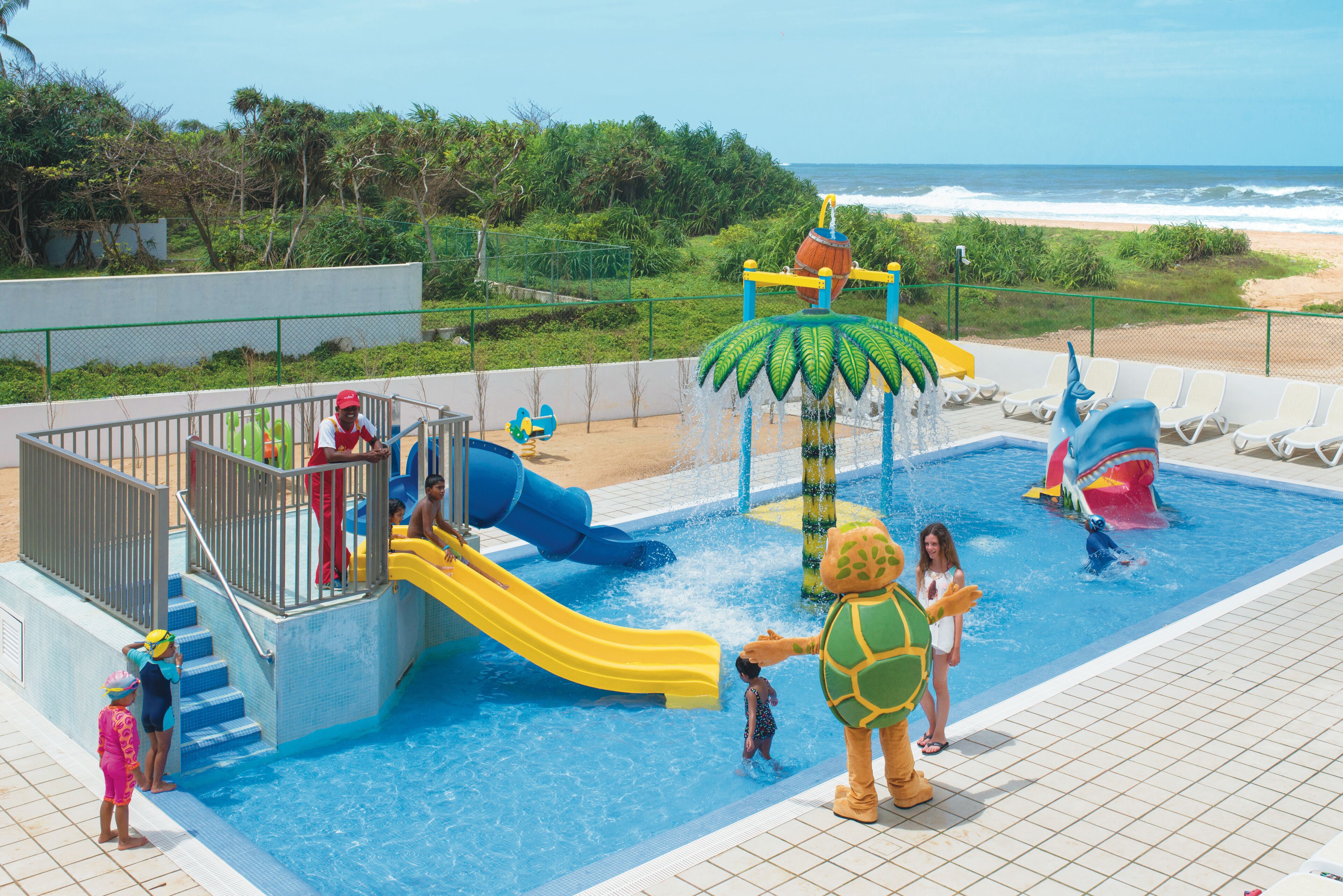 A water park with slides and a pool, surrounded by a fence and greenery.