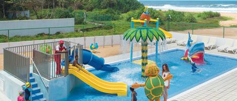 A water park with slides and a pool, surrounded by a fence and greenery.