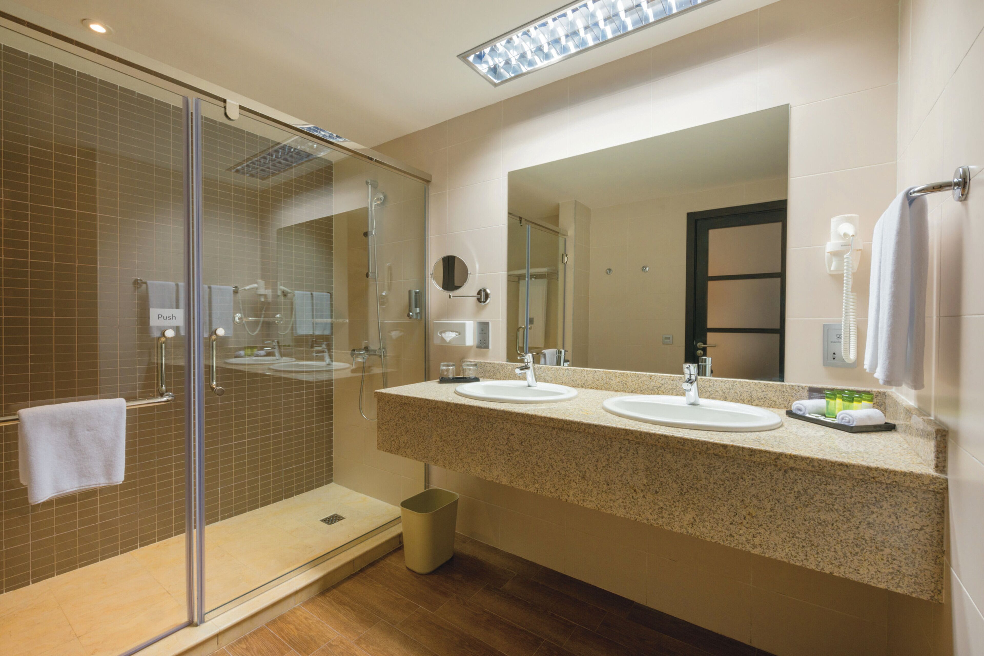 A modern bathroom with a glass-enclosed shower, two sinks, and a large mirror.
