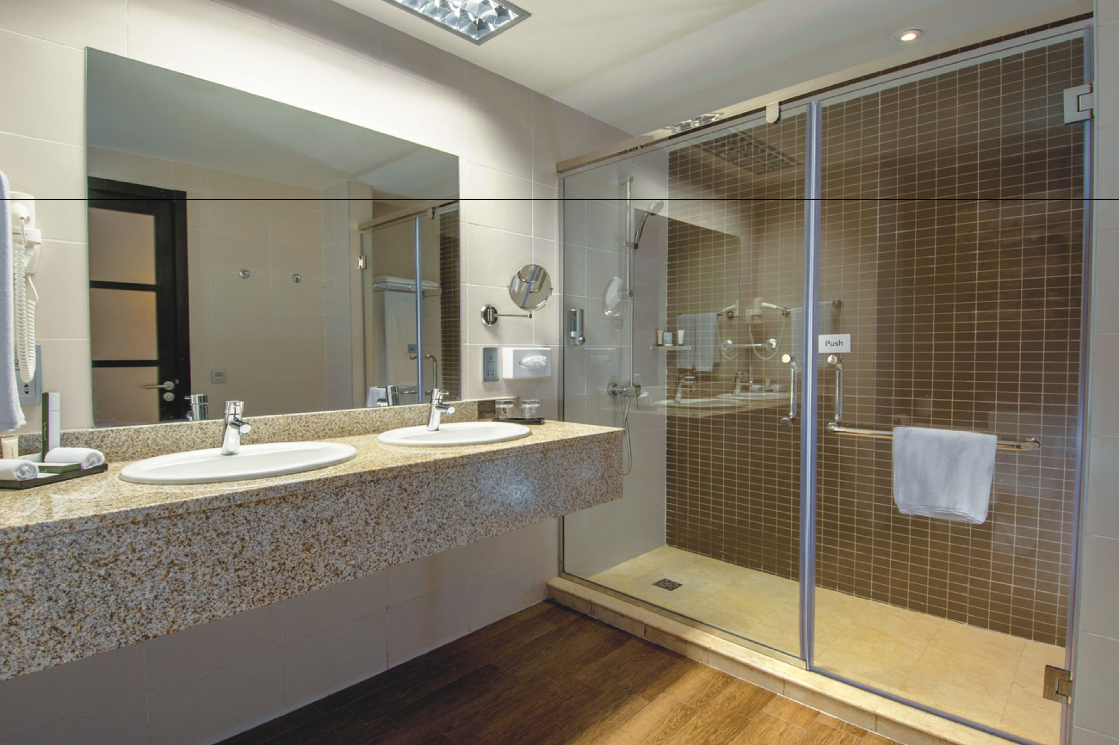A modern bathroom with two sinks, a large mirror, and a glass-enclosed shower area.