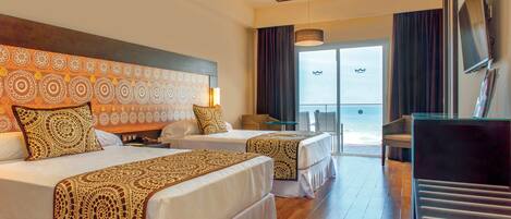 A hotel room with two beds, a desk, a TV, and a view of the ocean.