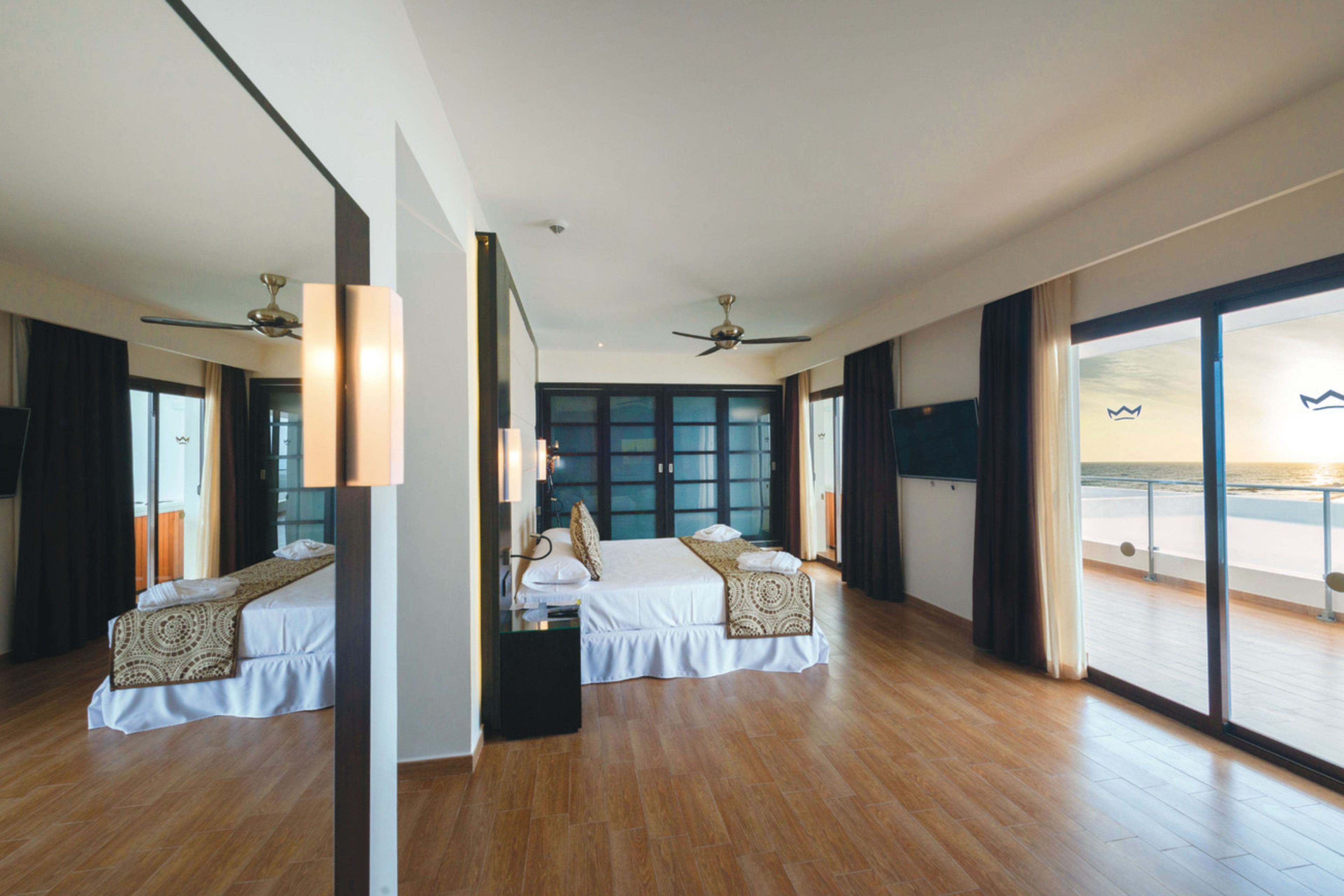 A modern hotel room with a large bed, a balcony with a view of the sea, and a ceiling fan.