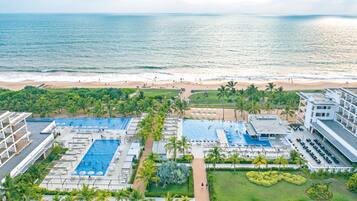 Een resort met meerdere zwembaden, een strand en palmbomen.