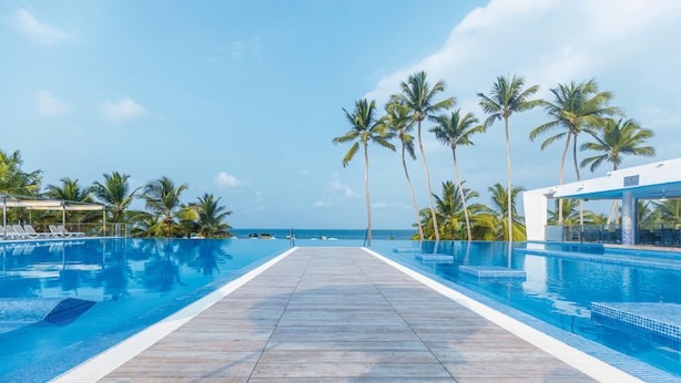 A pool area with clear blue water, a wooden deck, and palm trees. - Hotel Riu Sri Lanka - All Inclusive (Ahungalla)