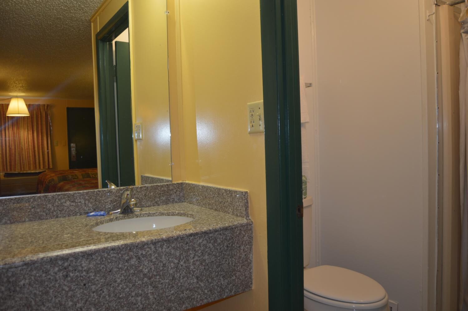 A bathroom with a granite countertop sink, a mirror, and a toilet.