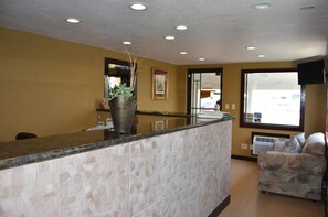 A reception area with a stone-textured counter, a potted plant, and a window with a view of the outside.