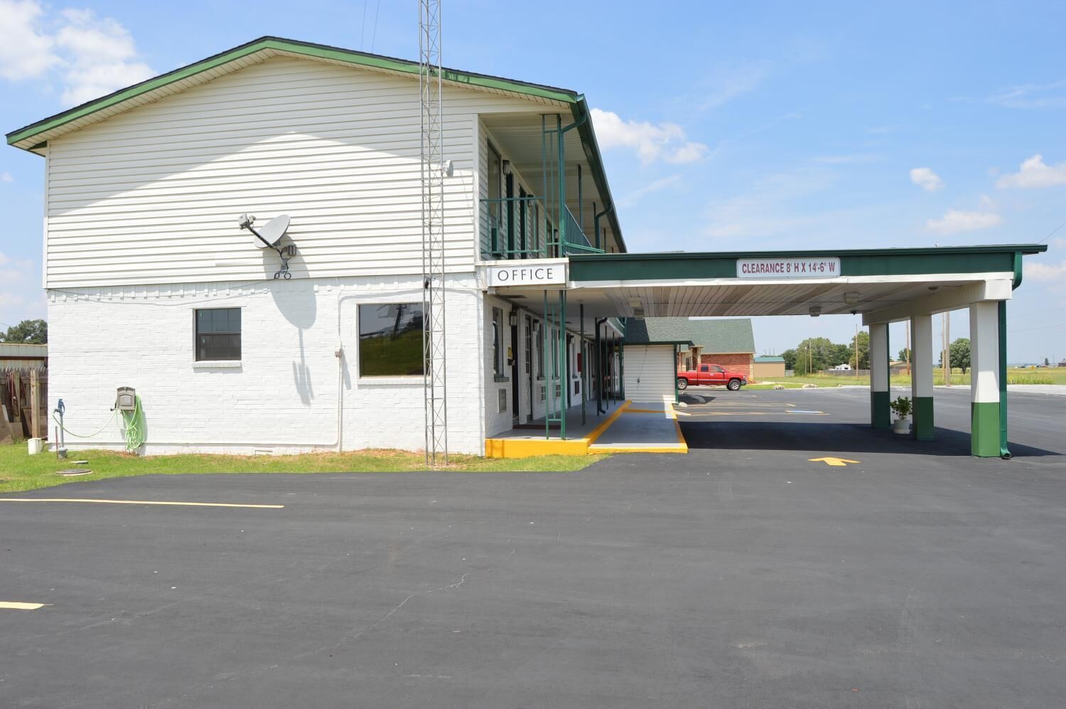 A small, single-story building with a white exterior and green trim. It has a covered entrance with a sign that reads "OFFICE" and "CLEARANCE & 14-8 W".