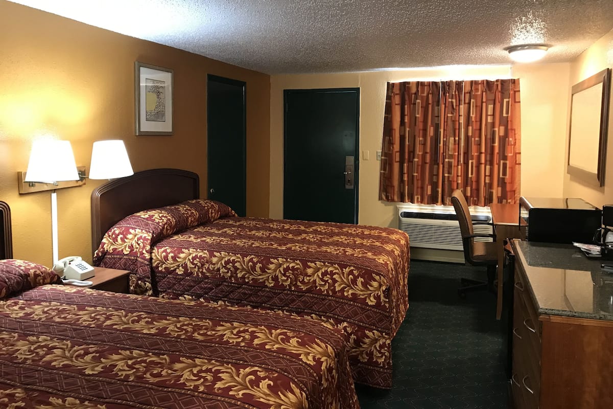 A hotel room with two beds, a desk, a chair, a telephone, and an air conditioning unit.