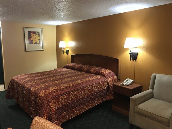 Quarto de hotel com uma cama grande, duas luminárias laterais, um telefone, uma cadeira e um quadro na parede.