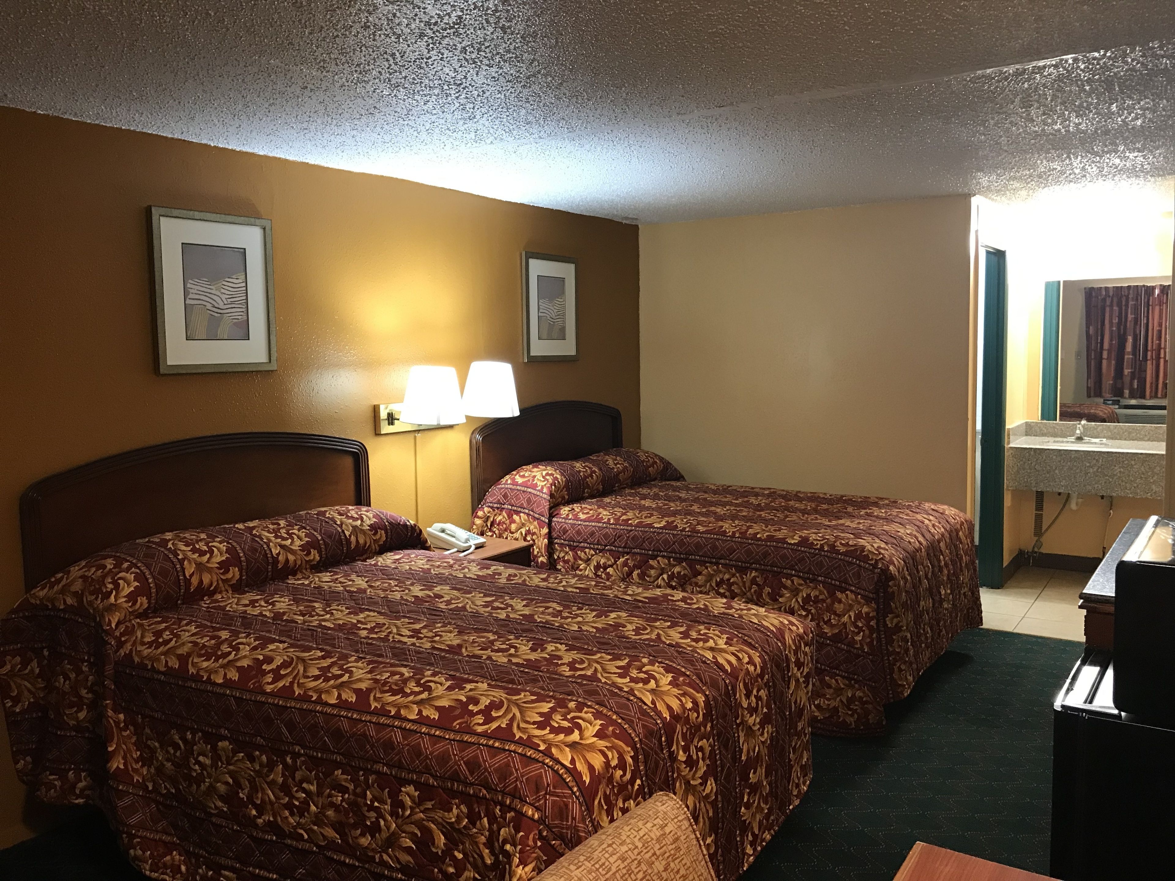 Une chambre d’hôtel avec deux lits, une table de chevet, une lampe et une salle de bain visible à travers une porte ouverte.