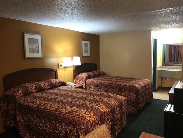 A hotel room with two beds, a nightstand, a lamp, and a bathroom visible through an open door.