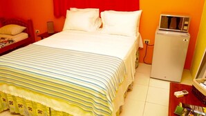 A hotel room with a bed, a small refrigerator, and a nightstand with a lamp. - Angel Fish Cove (Buccoo)