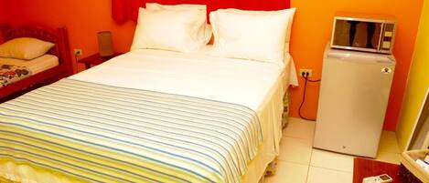 Habitación de hotel con cama, un refrigerador pequeño y una mesita de noche con lámpara.