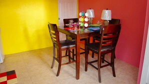 A dining area with a wooden table and four chairs, a white door, and a red wall. - Angel Fish Cove (Buccoo)