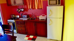 A compact kitchen with a stove, toaster, sink, and a microwave on top of a refrigerator. - Angel Fish Cove (Buccoo)