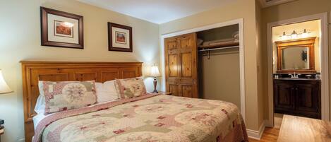 A bedroom with a wooden headboard, a quilted bedspread, a nightstand with a lamp, and a wooden dresser.