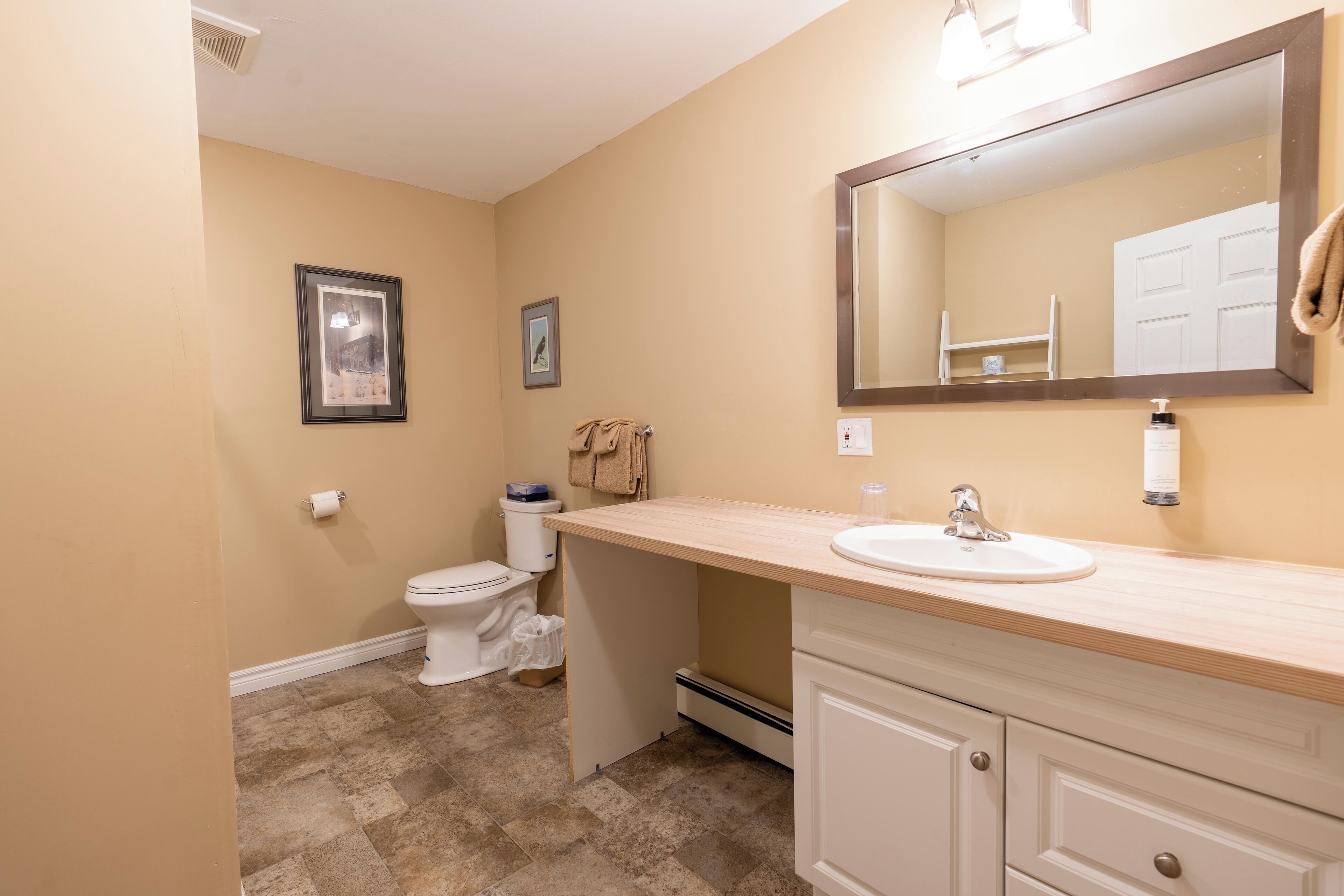 A bathroom with a beige wall, a white toilet, a sink with a mirror, and a towel hanging on the wall.