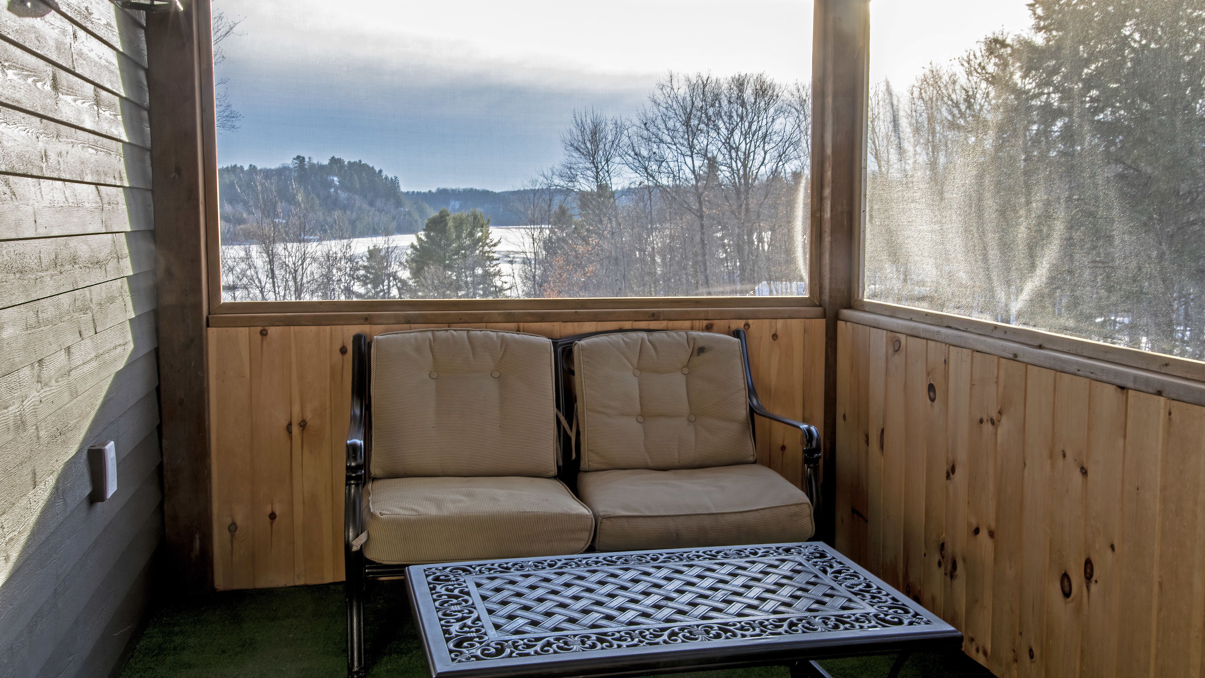 A wooden porch with two cushioned chairs and a metal table.