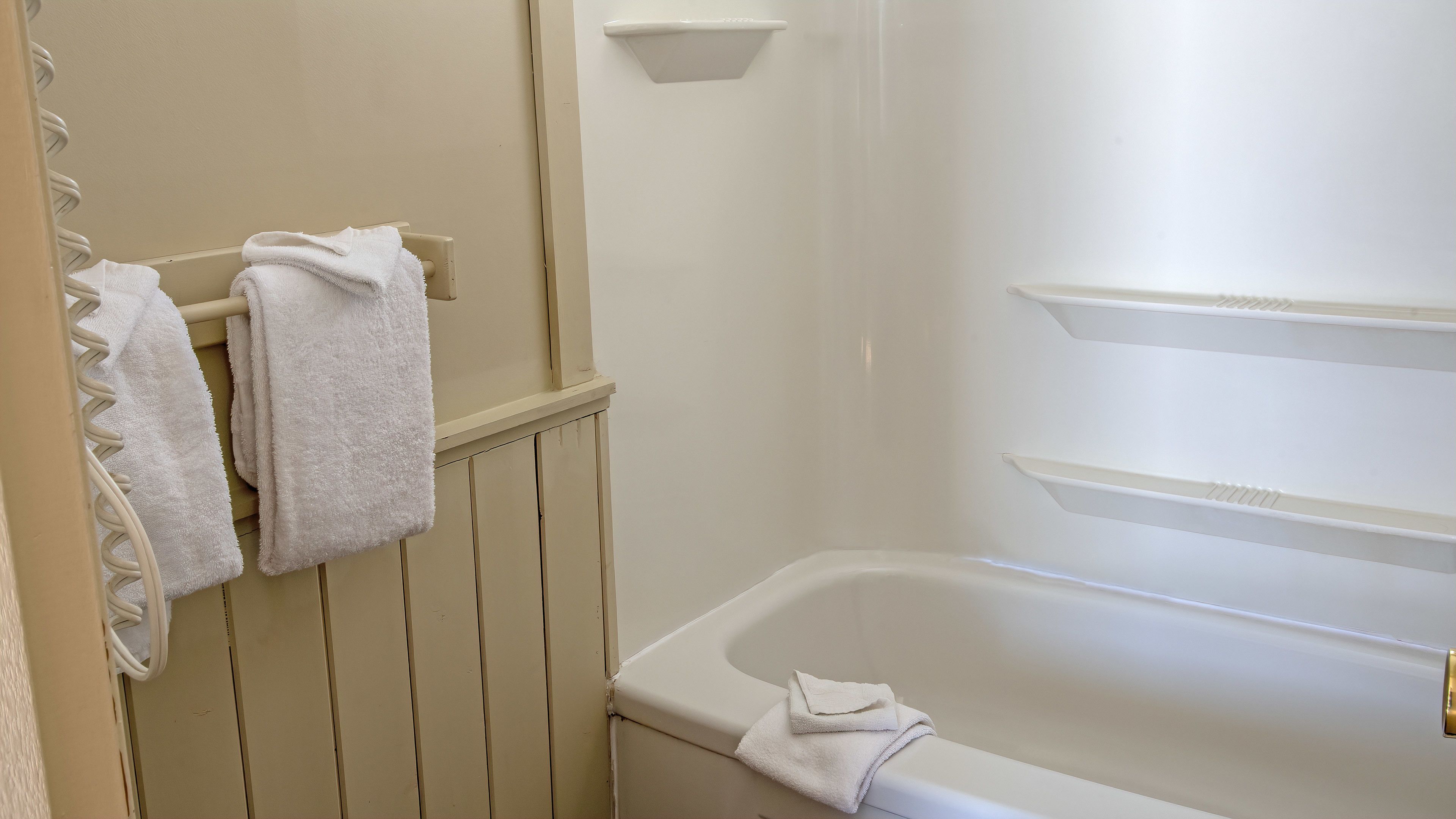 A bathroom with a bathtub, a towel rack with towels, and a white wall.