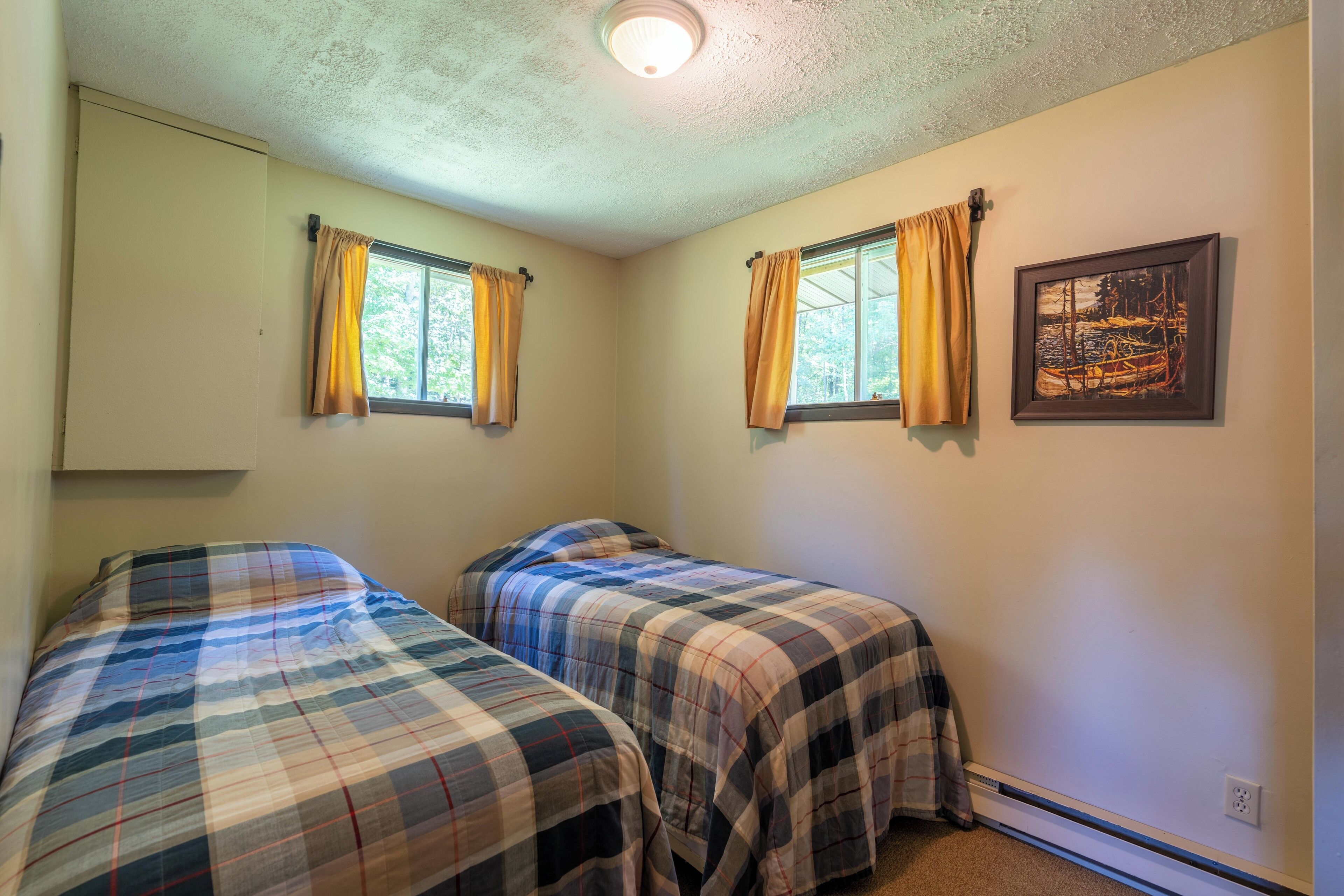 Une chambre avec deux lits, un luminaire au plafond et un tableau accroché au mur.