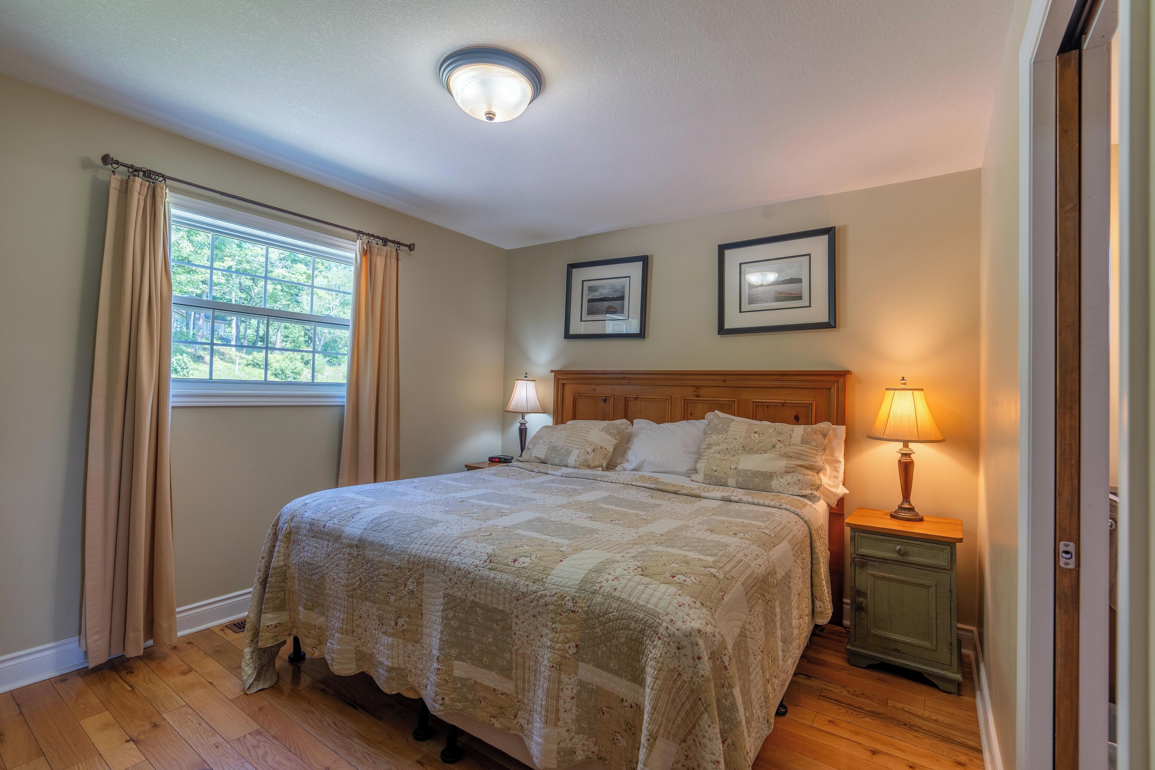 A bedroom with a large bed, two bedside lamps, a wooden headboard, and two framed pictures on the wall.