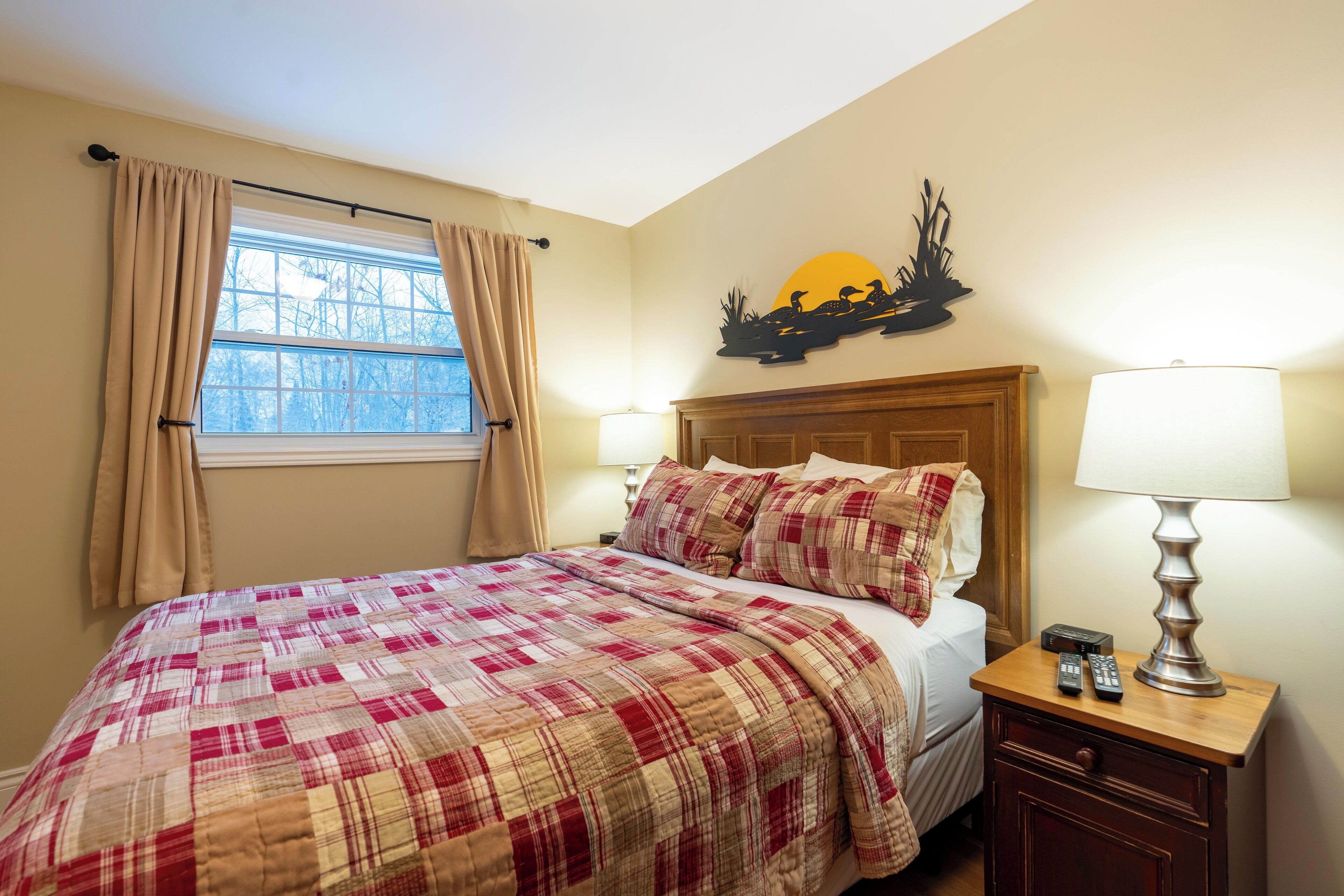 Une chambre à coucher comprenant un lit, une table de chevet, une lampe, une fenêtre avec des rideaux et un élément de décoration murale.