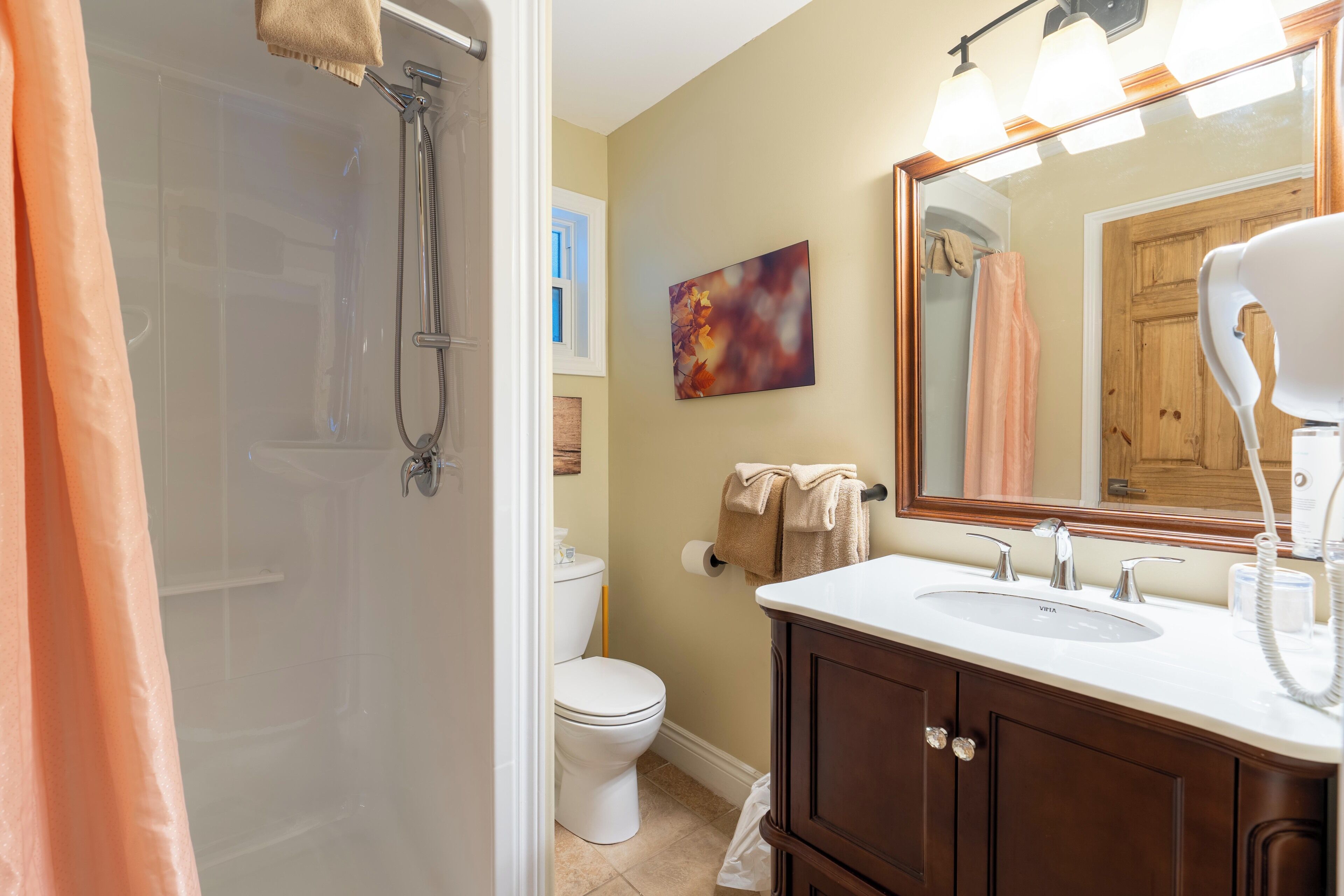 A bathroom with a shower, toilet, sink, and a large mirror.