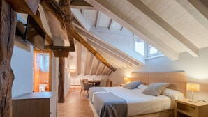 A bedroom with a sloped ceiling, wooden beams, a bed with pillows, a bedside table, and a desk. - Apartamentos Posada La Robla (Castaneda)