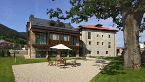 A two-story building with a modern design, featuring a patio area with outdoor seating and a large umbrella. - Apartamentos Posada La Robla (Castaneda)