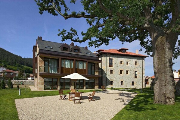 A two-story building with a modern design, featuring a patio area with outdoor seating and a large umbrella. - Apartamentos Posada La Robla (Castaneda)