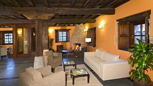 A cozy living room with a fireplace, comfortable seating, and a large window. - Apartamentos Posada La Robla (Castaneda)