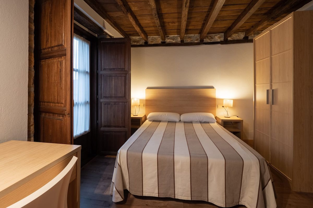 Un dormitorio con cabecera de madera, cama con ropa de cama a rayas, dos lámparas de noche y un armario de madera.