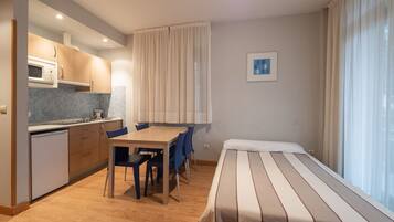 Een kleine hotelkamer met kitchenette, eettafel en bed.