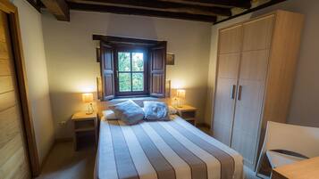 A bedroom with a large bed, two bedside tables with lamps, a window with a view of greenery, and a wardrobe.