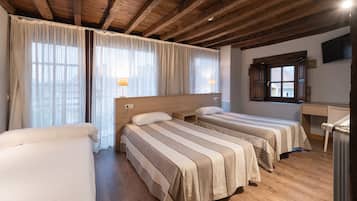 Quarto de hotel com duas camas, vigas de madeira no teto, uma escrivaninha e uma janela com cortinas.