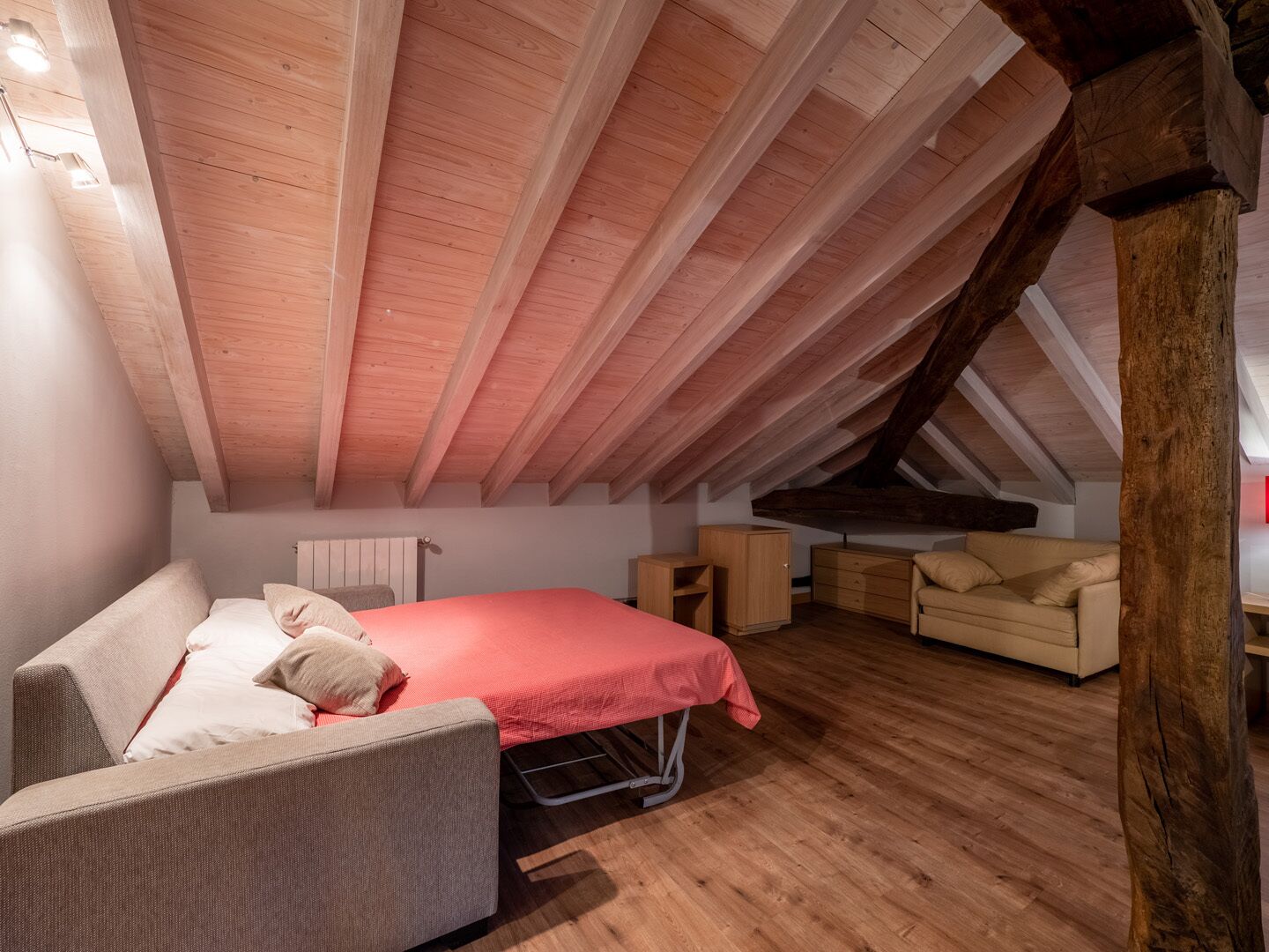 Een knus zolderkamer met een schuine kap, een bed, een slaapbank en een dressoir.