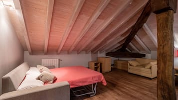 Een knus zolderkamer met een schuine kap, een bed, een slaapbank en een dressoir.