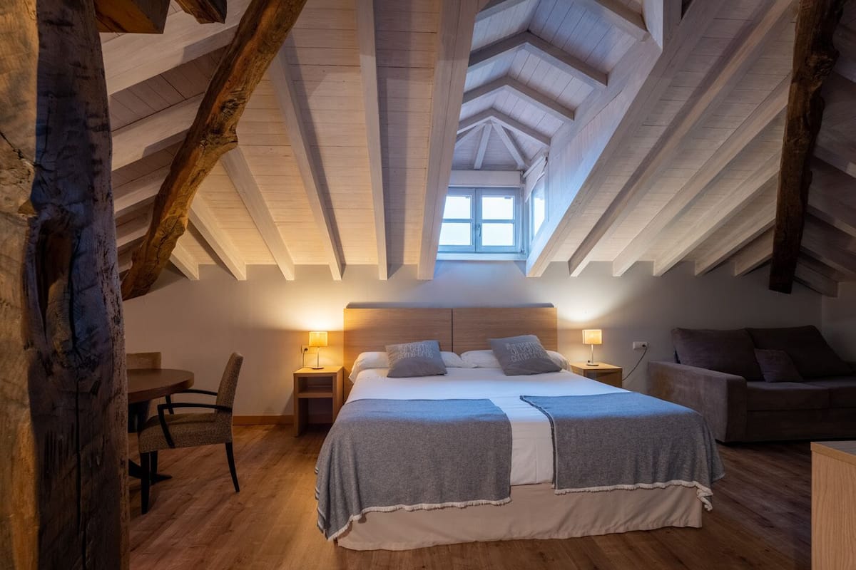 Un dormitorio acogedor en el ático con una cama grande, vigas de madera y un tragaluz.